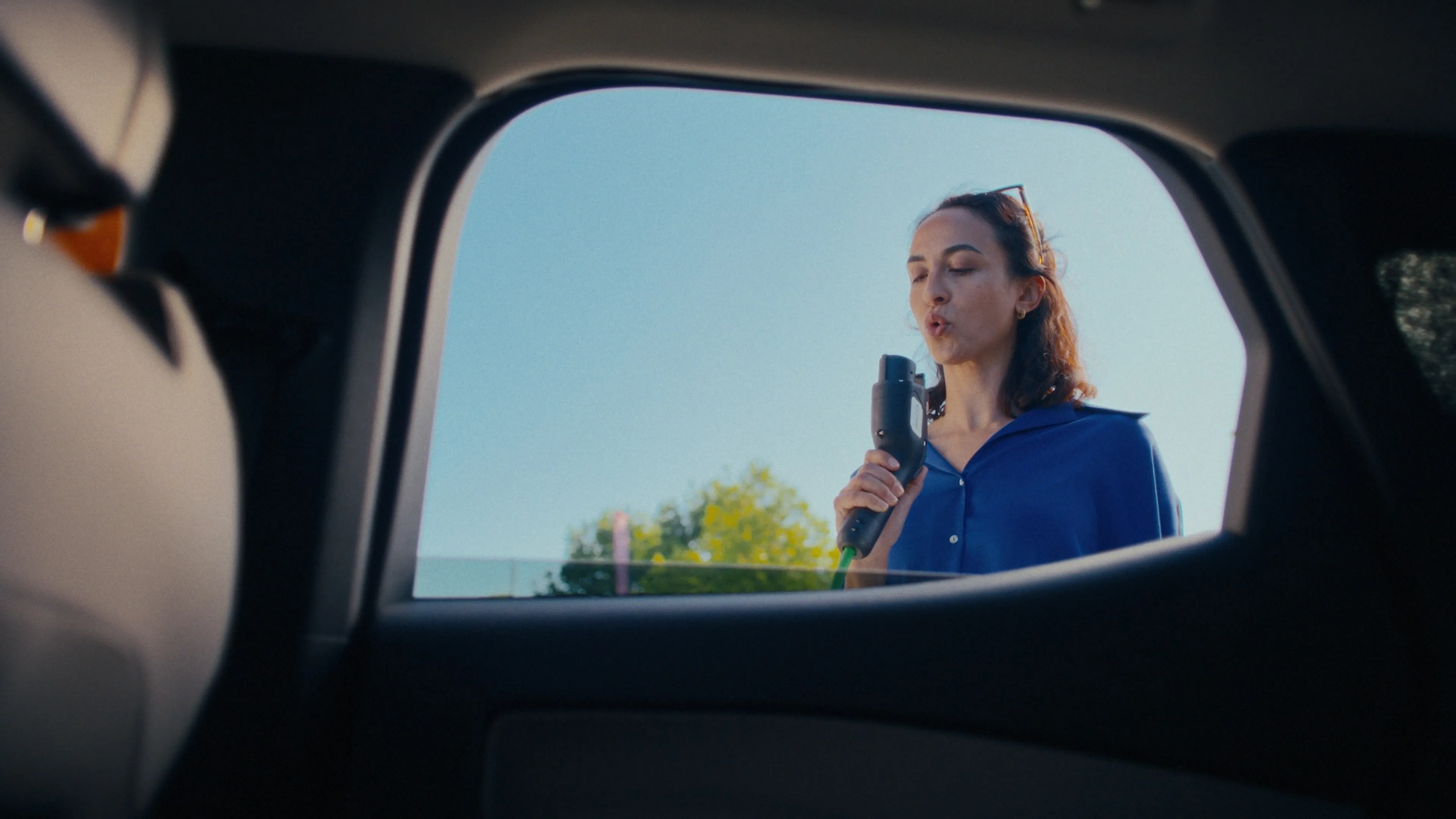 View from inside a car of a person connecting a charging cable to an electric vehicle.