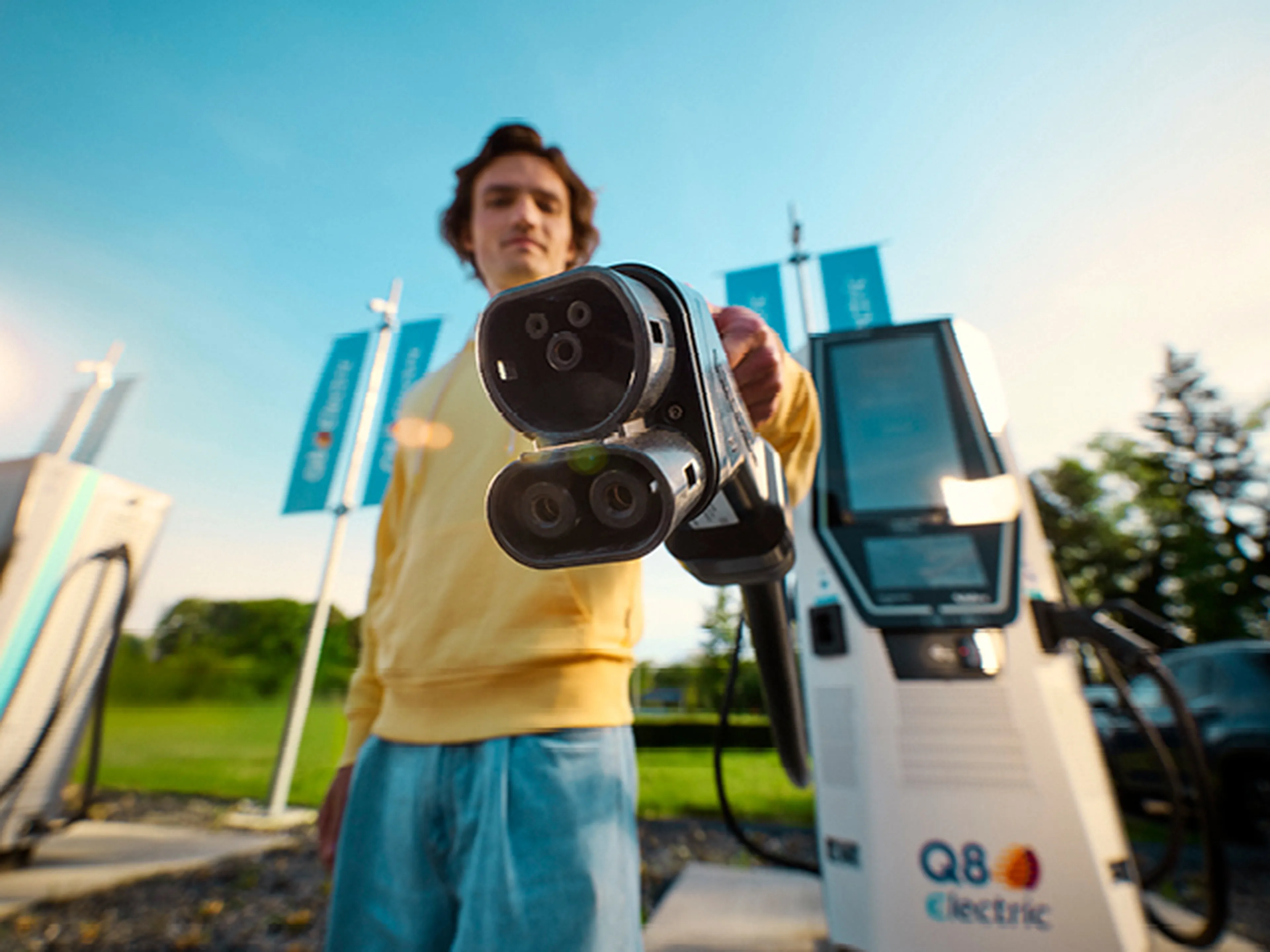 Person holding an electric vehicle charging connector in front of a Q8 electric fast charging station.